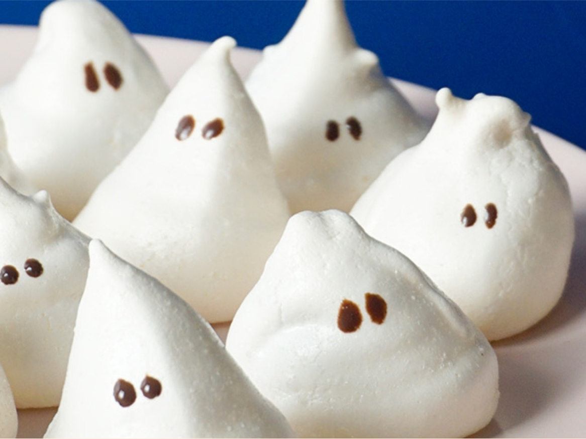 Meringues brancos em forma de fantasma com olhos de chocolate num prato.
