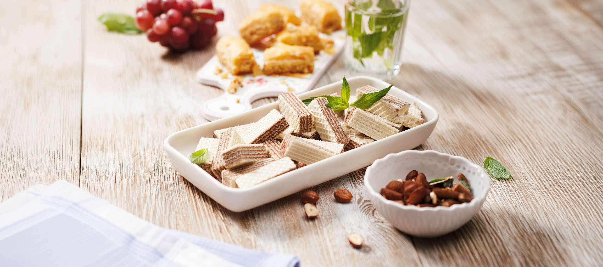 Bolachas wafer, baklava, uvas e água de menta numa mesa de madeira.