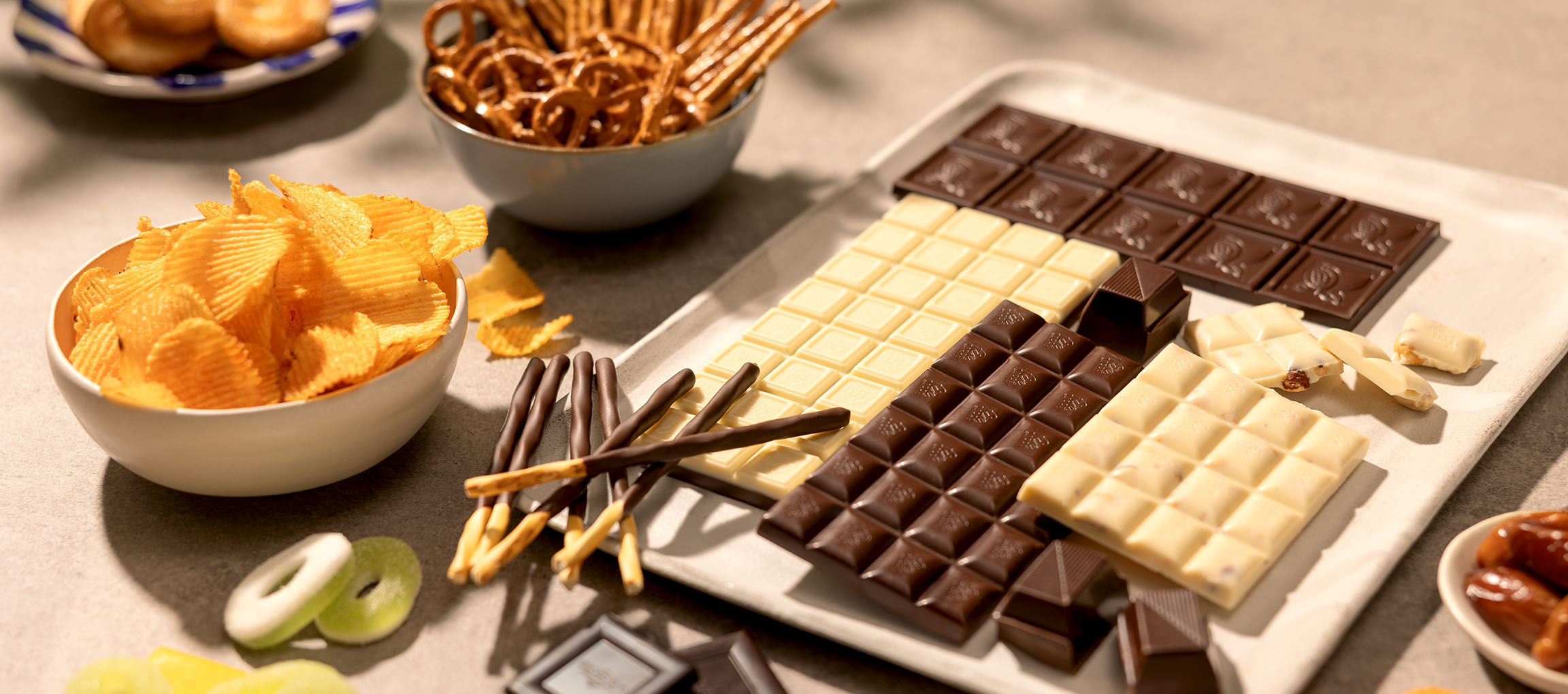 Chocolates variados, batatas fritas, pretzels e doces numa mesa.