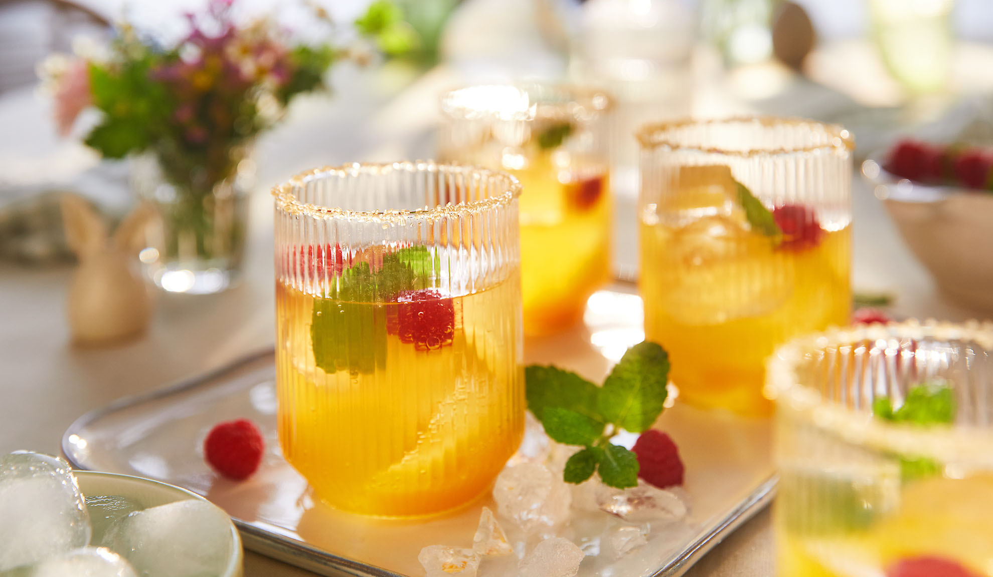 Bebidas refrescantes de verão com framboesas e hortelã, servidas numa bandeja com gelo.