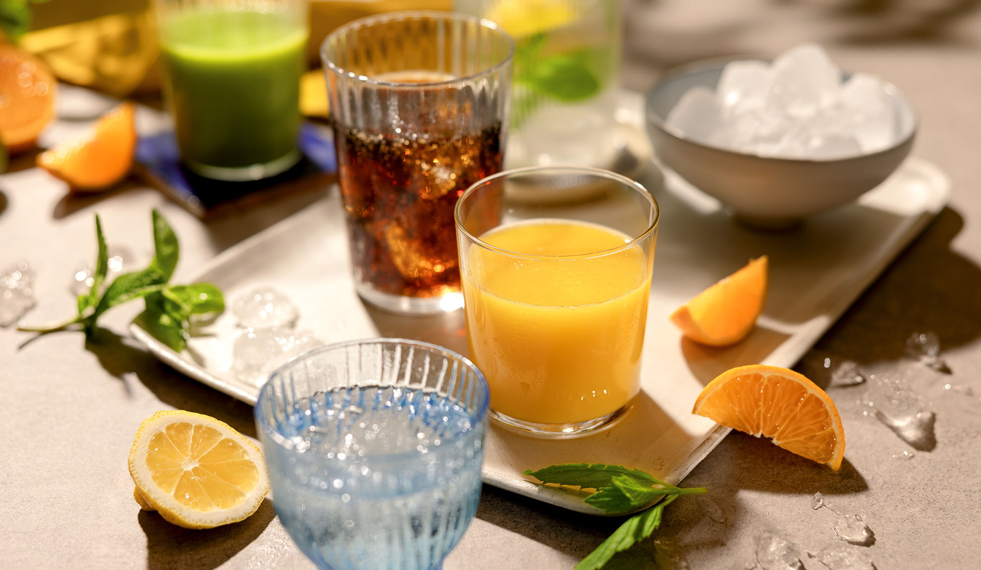 Várias bebidas refrescantes com gelo, fatias de citrinos e hortelã numa bandeja.
