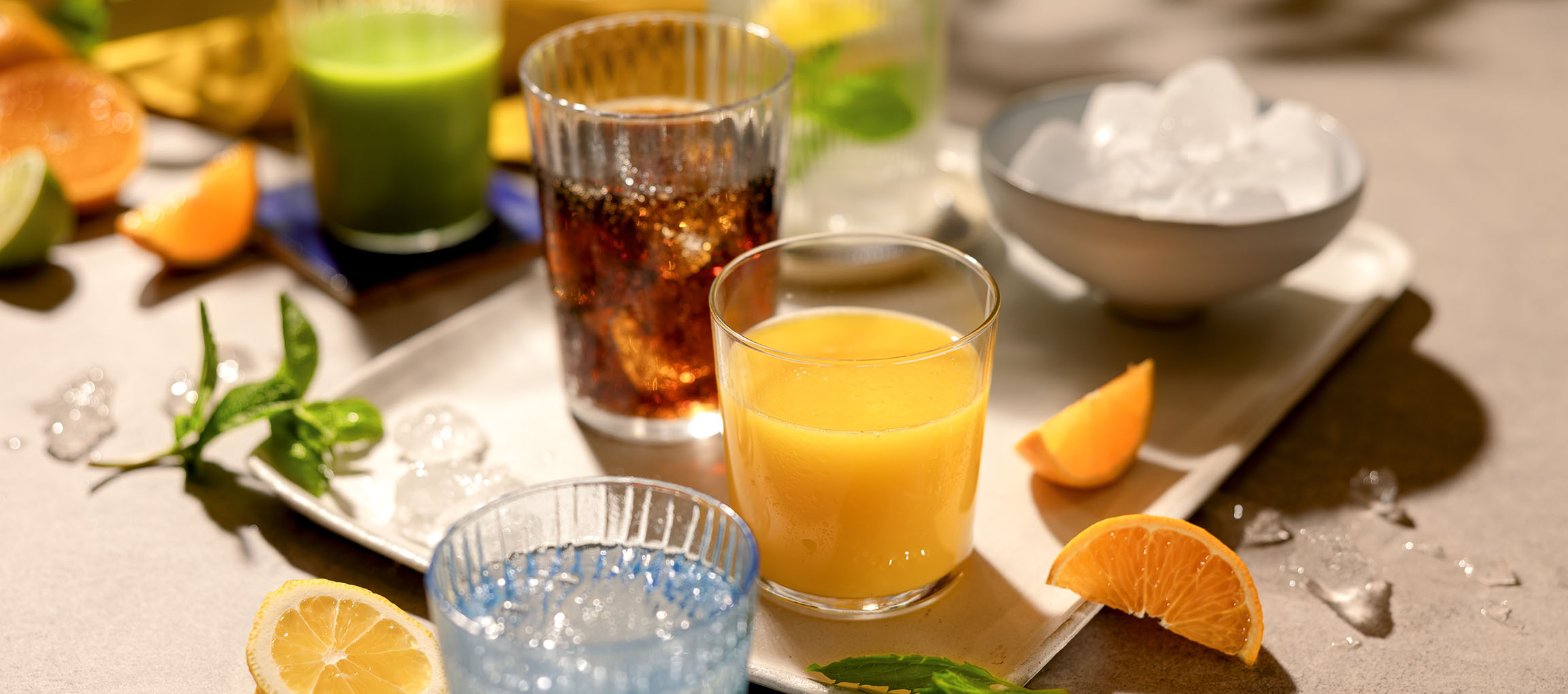 Várias bebidas refrescantes e frutas numa bandeja, incluindo sumo de laranja e bebidas gaseificadas.