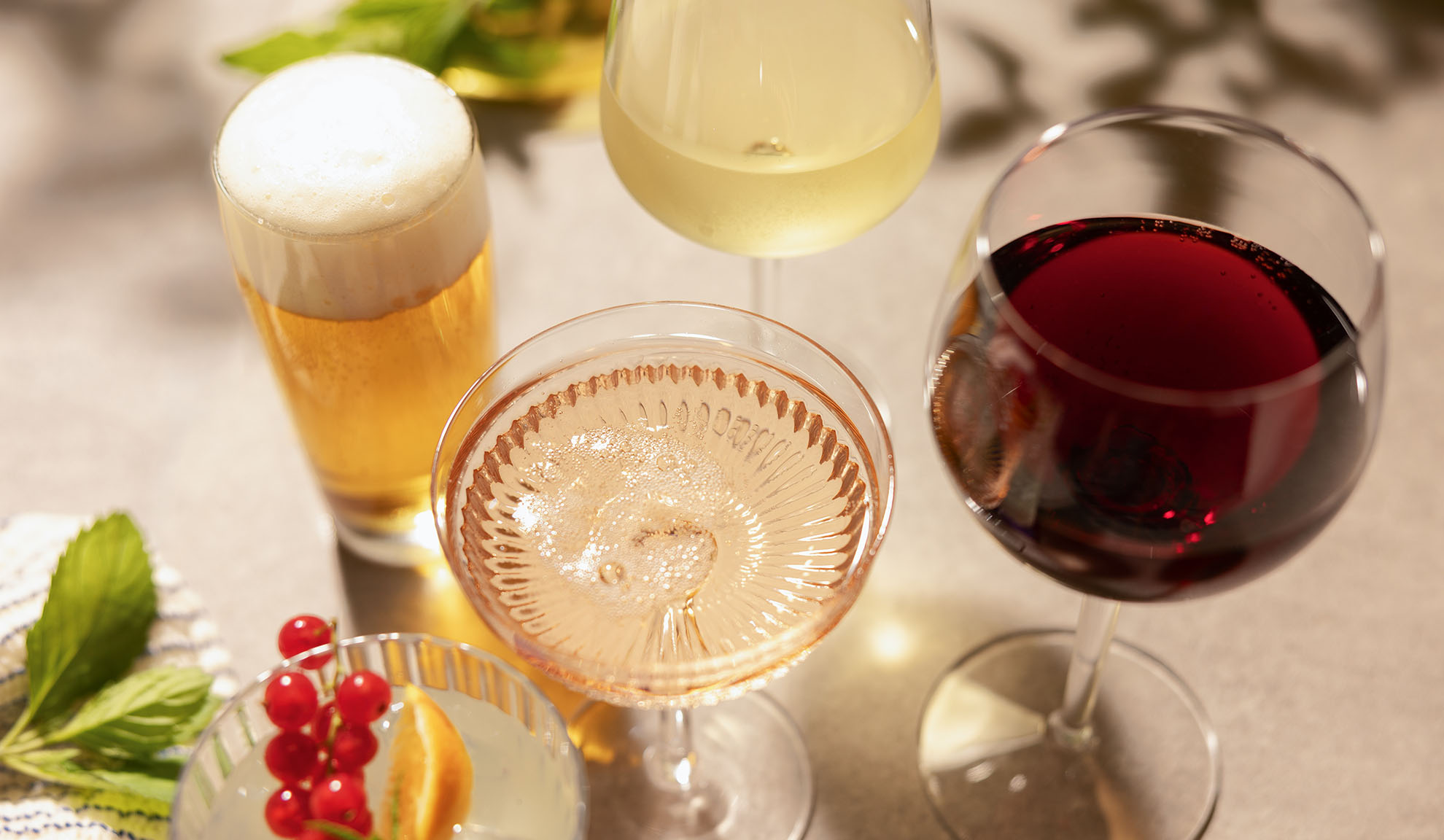 Copos de cerveja, vinho branco, rosé e tinto, com um cocktail e bagas.