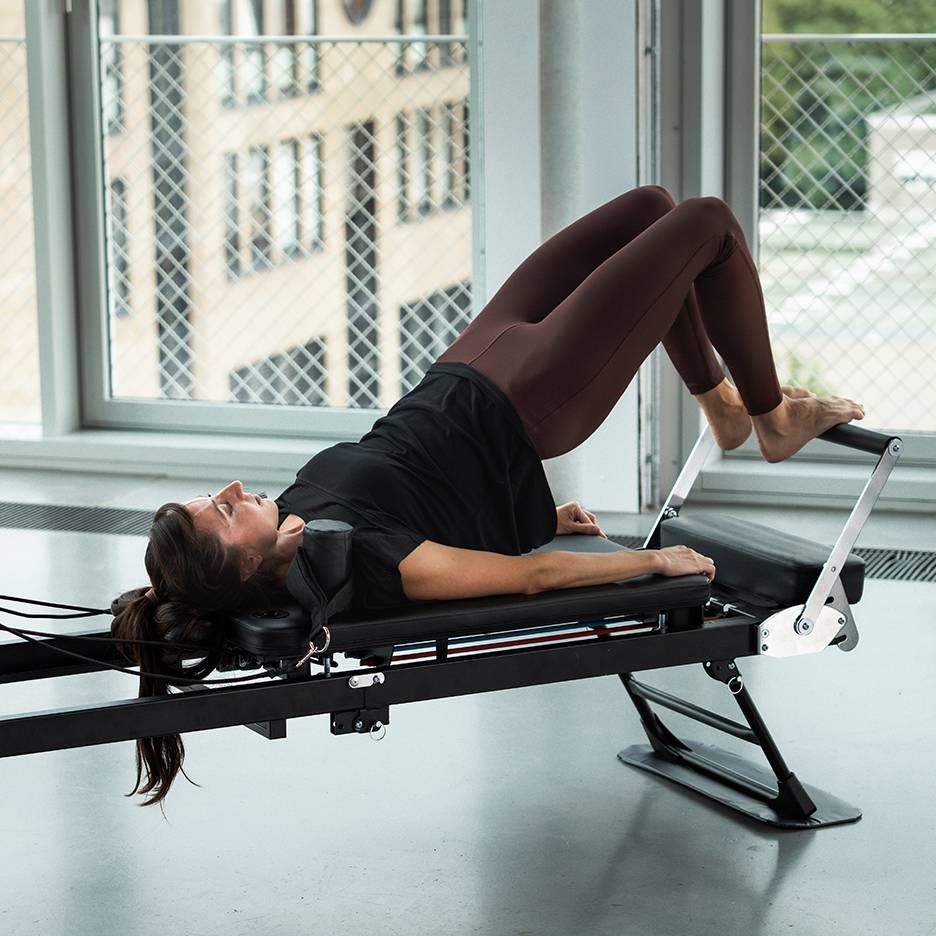 Mulher a fazer Pilates numa máquina reformer, com as pernas para cima.
