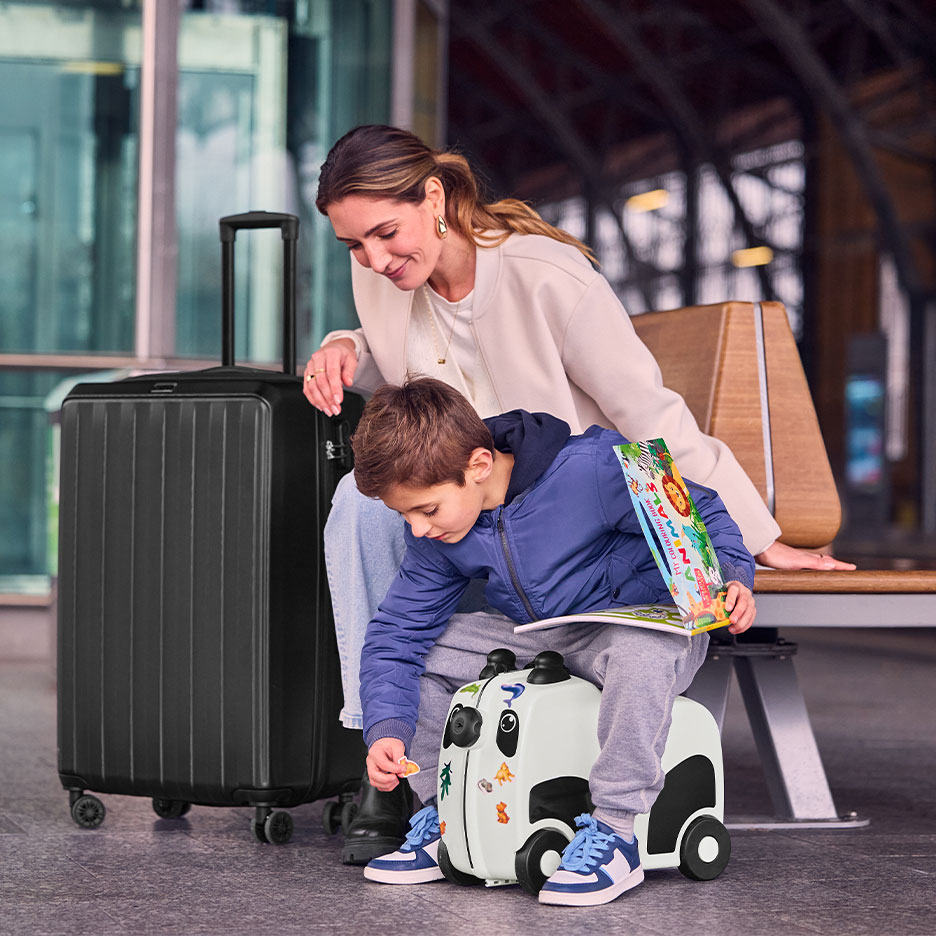Mulher e criança com mala preta grande e mala de viagem panda num aeroporto.