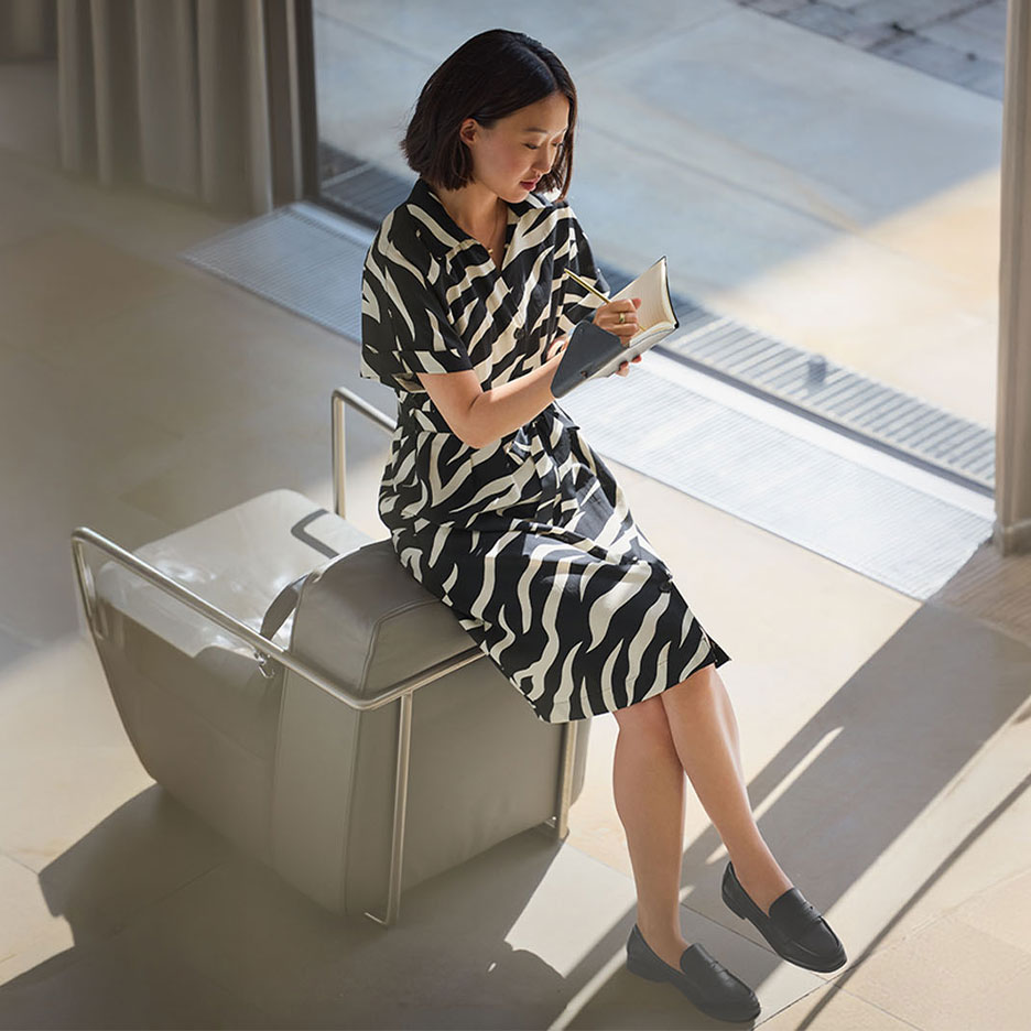 Mulher com vestido estampado de zebra e mocassins, a escrever num caderno.