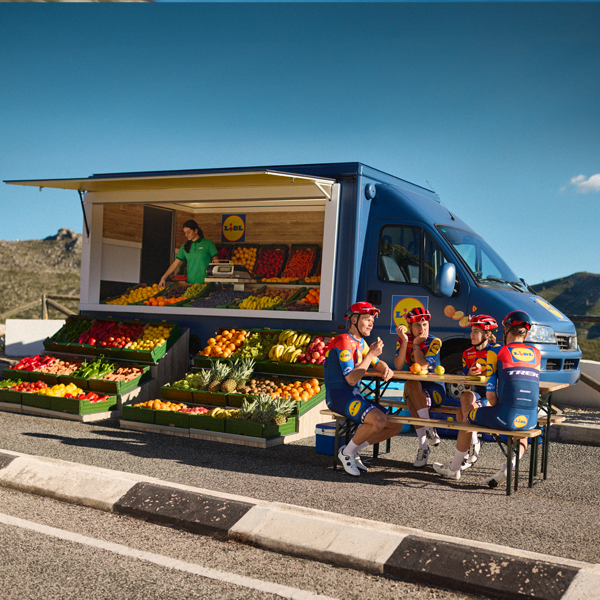 Ciclistas descansam perto de um camião Lidl cheio de frutas e legumes.