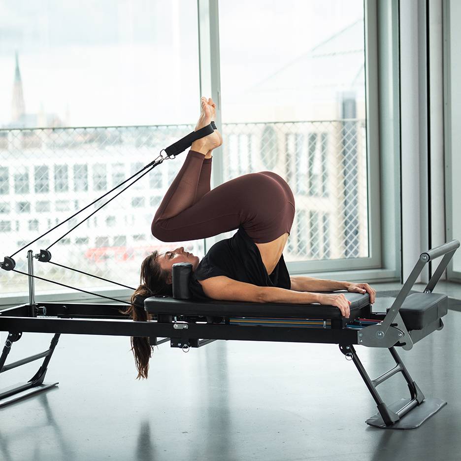 Mulher a fazer Pilates num reformer com as pernas para cima e os pés nas correias.