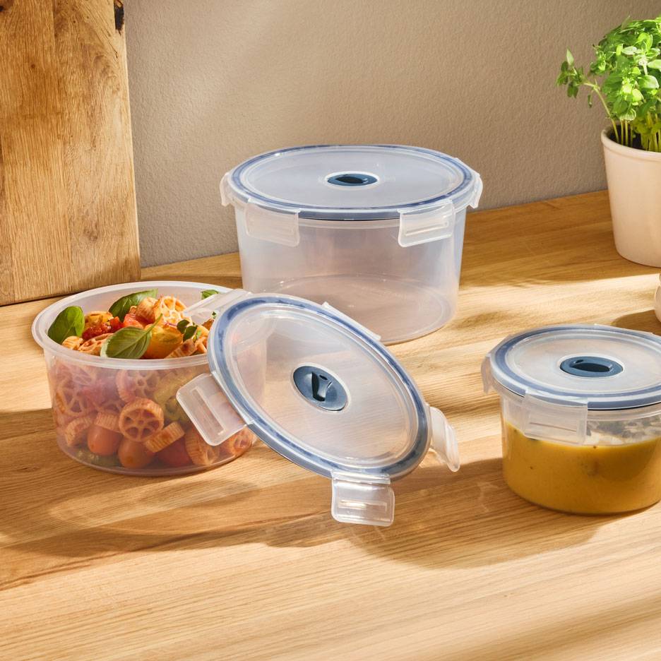 Recipientes redondos transparentes para alimentos com tampas de aro azul, um com salada de massa, outro com sopa.