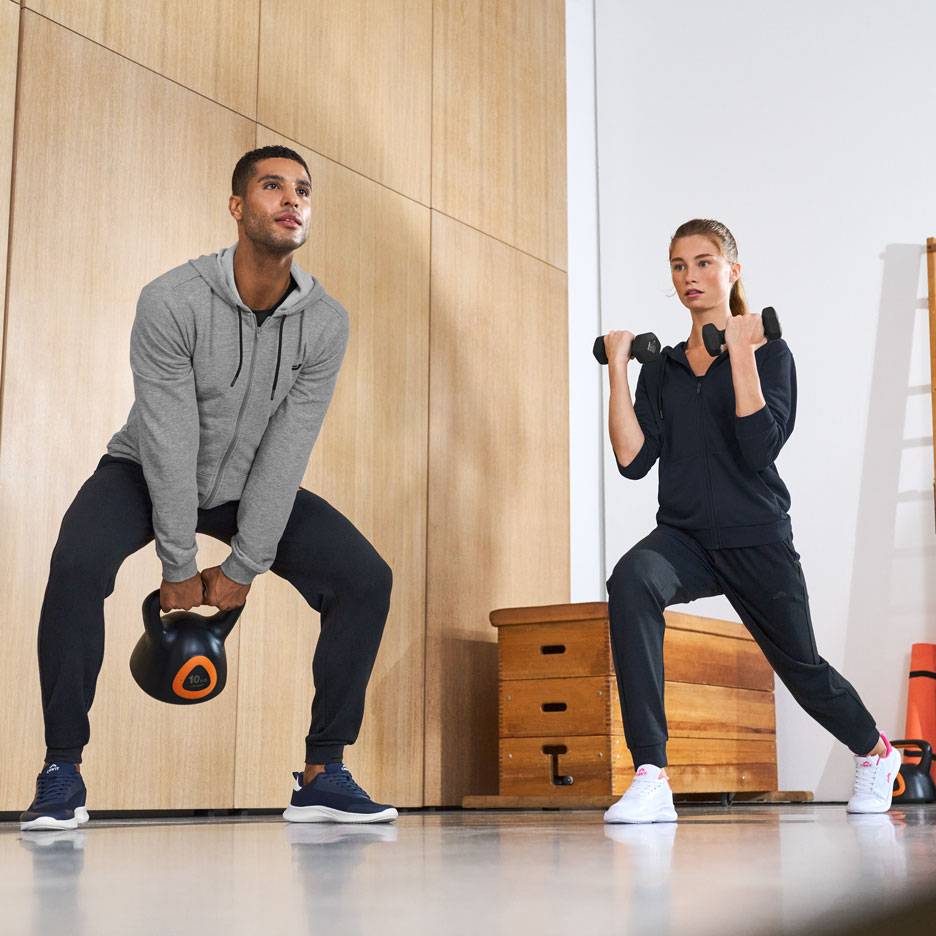 Homem e mulher em roupa desportiva, a treinar com um kettlebell e halteres.
