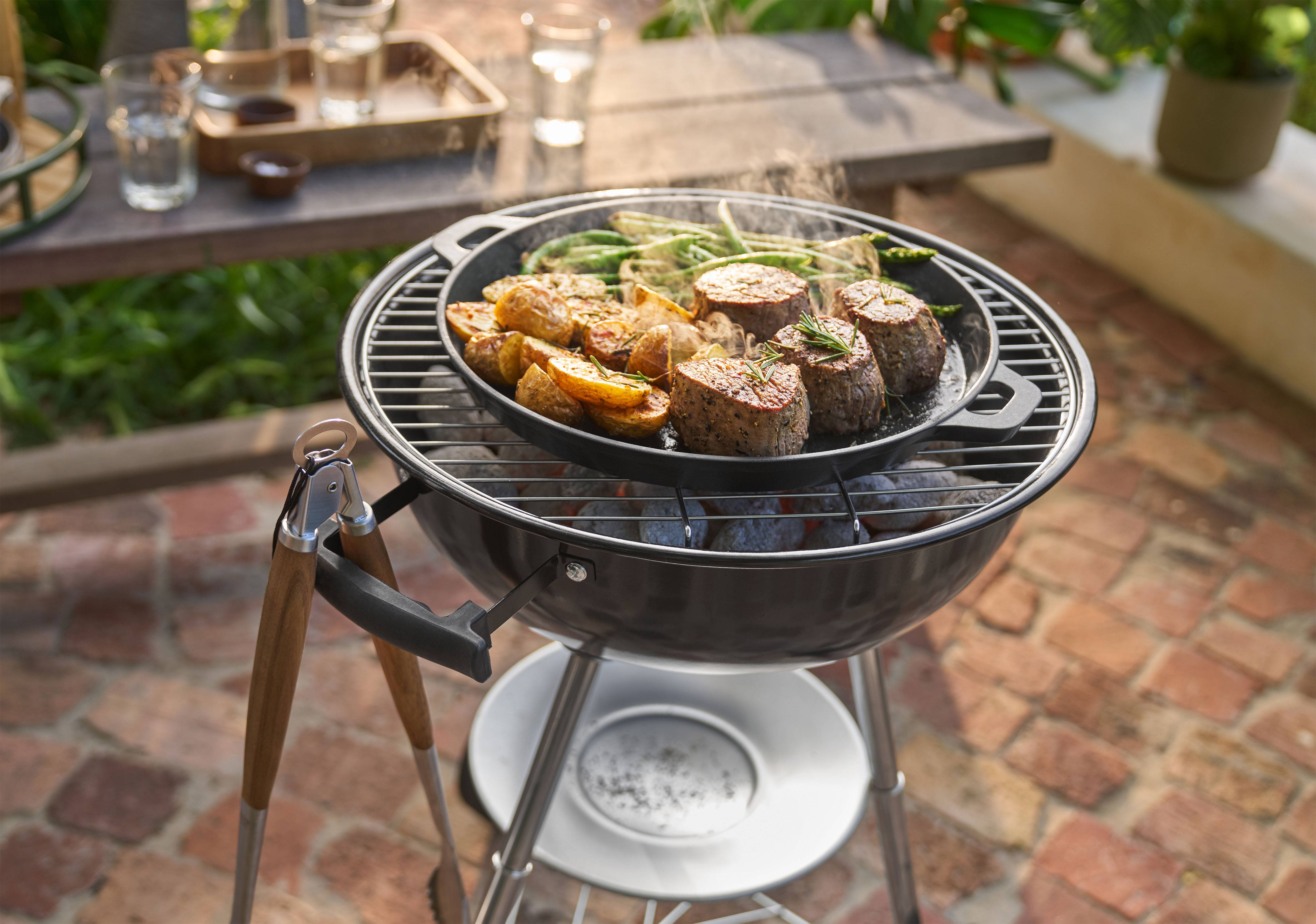 Churrasco com carne, batatas e feijão verde a cozinhar numa frigideira ao ar livre.