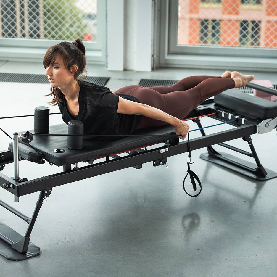 Mulher a exercitar-se numa máquina de Pilates com bandas de resistência.