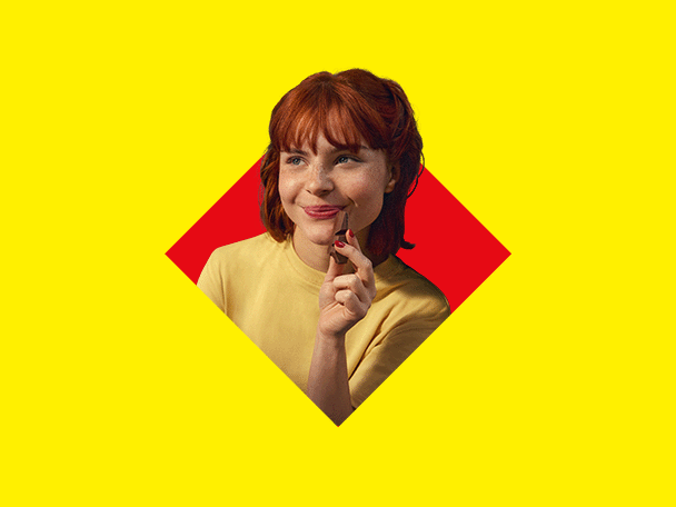 Uma mulher ruiva sorridente segurando um chocolate em um fundo amarelo e vermelho.