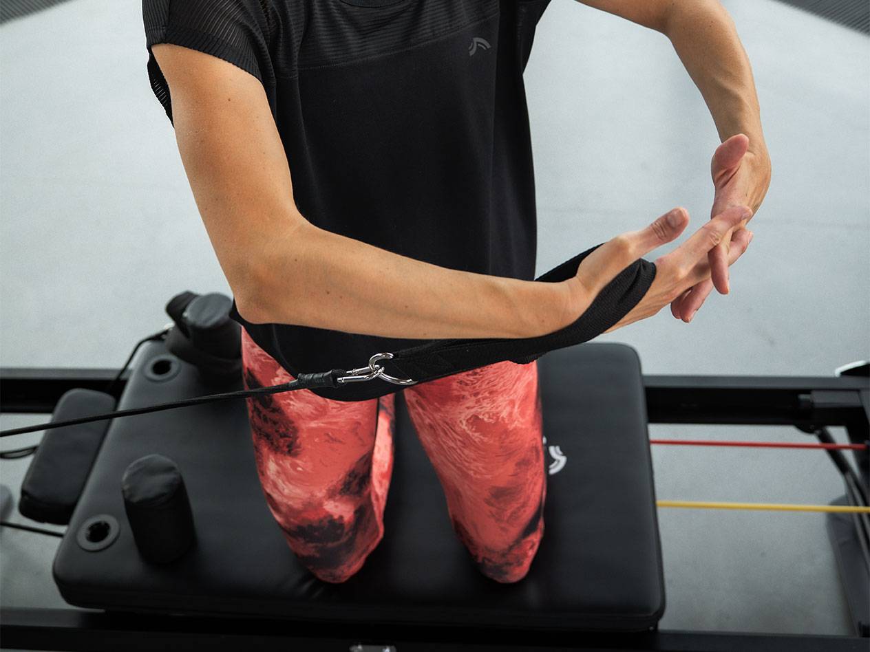 Mulher a exercitar-se com bandas de resistência numa máquina de Pilates.