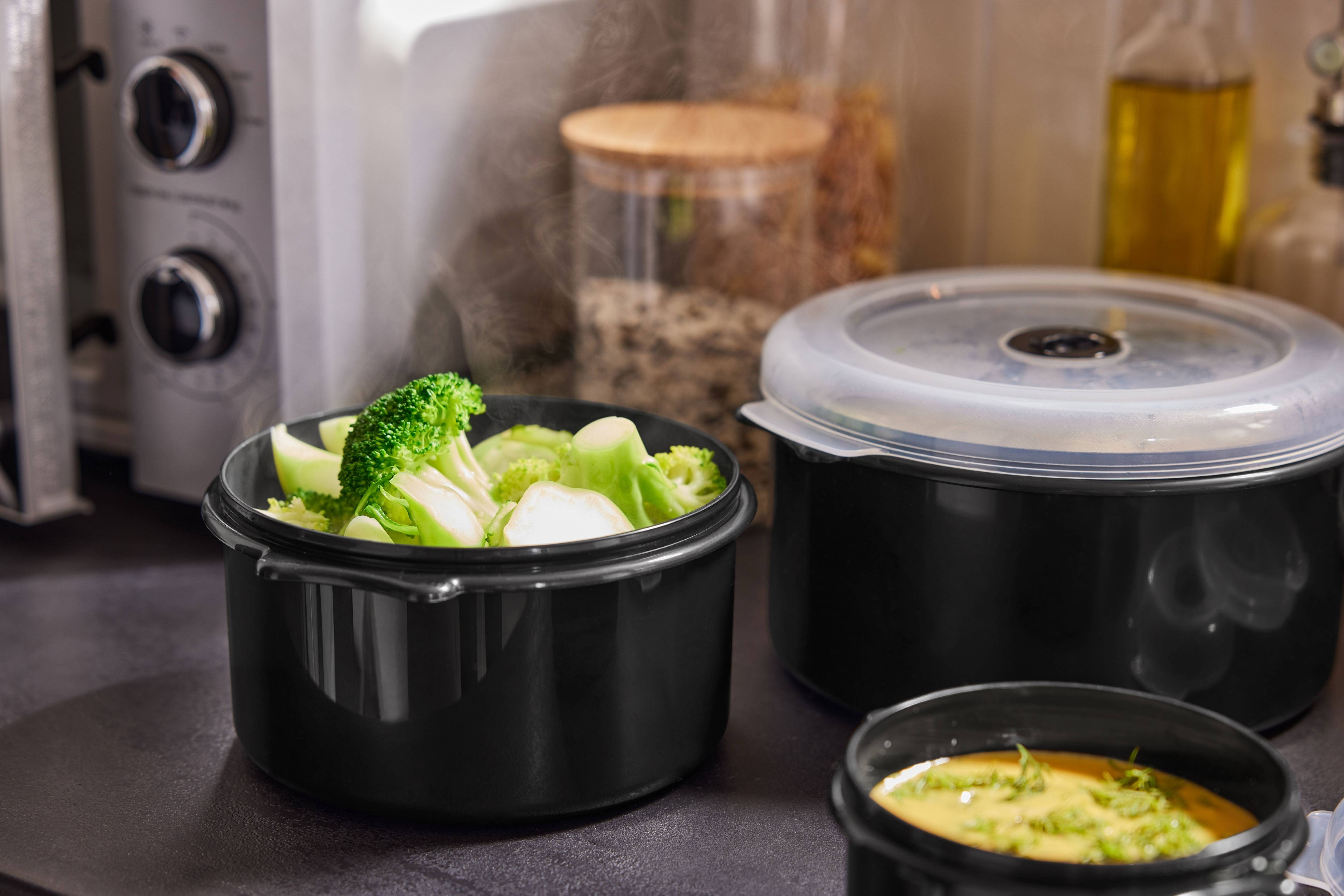 Brócolos a vapor e outros pratos em recipientes pretos na bancada da cozinha.