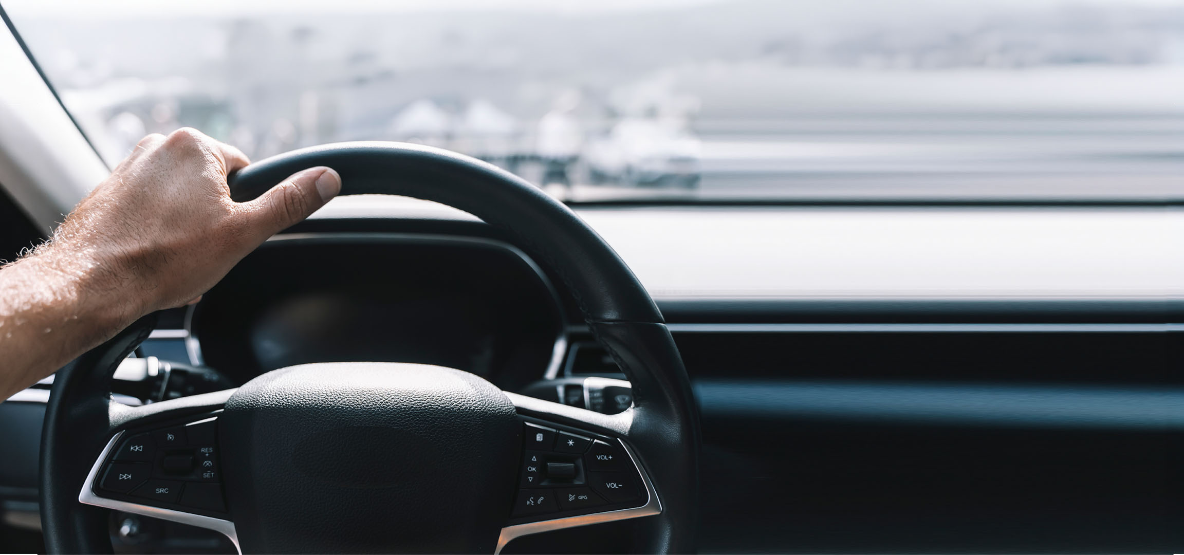Mão de um homem a segurar o volante de um carro.