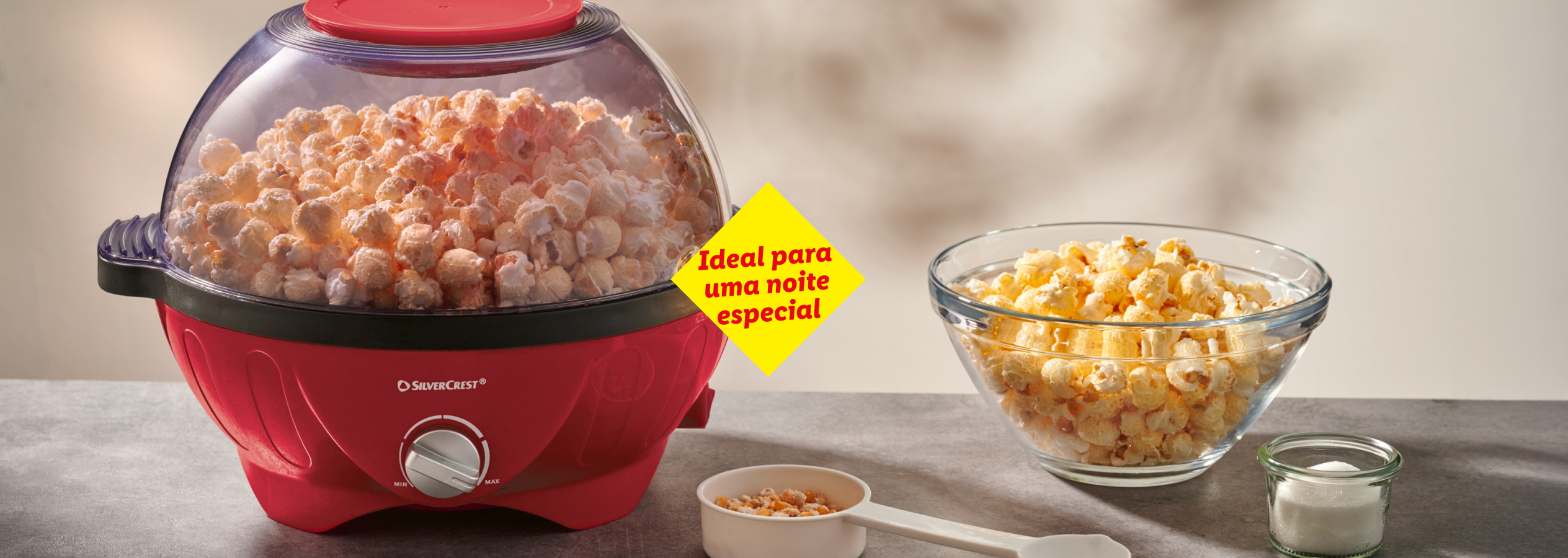 Máquina de pipocas SilverCrest vermelha com pipocas, tigela de pipocas e medidor de milho. 'Ideal para uma noite especial'.