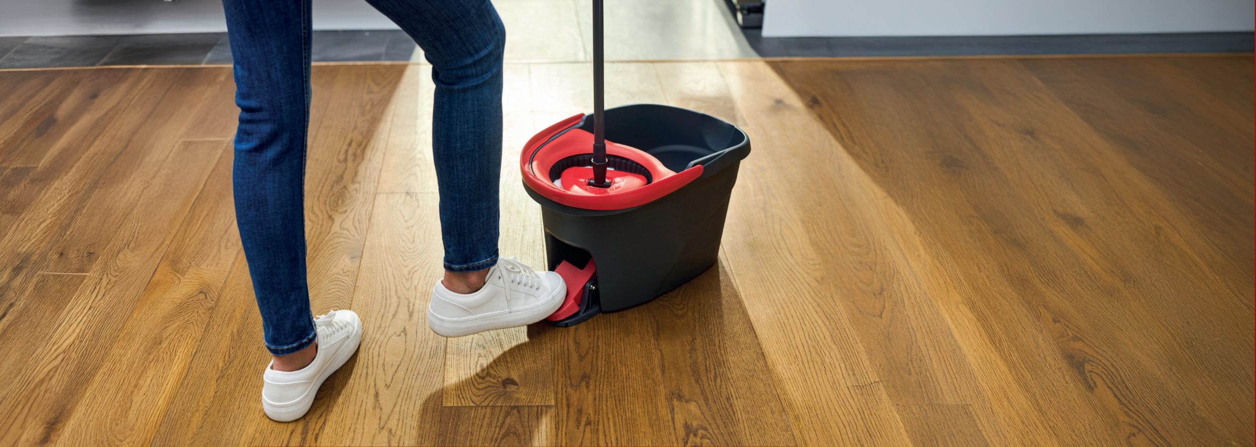 Pessoa a usar um balde e esfregona para limpar um chão de madeira.