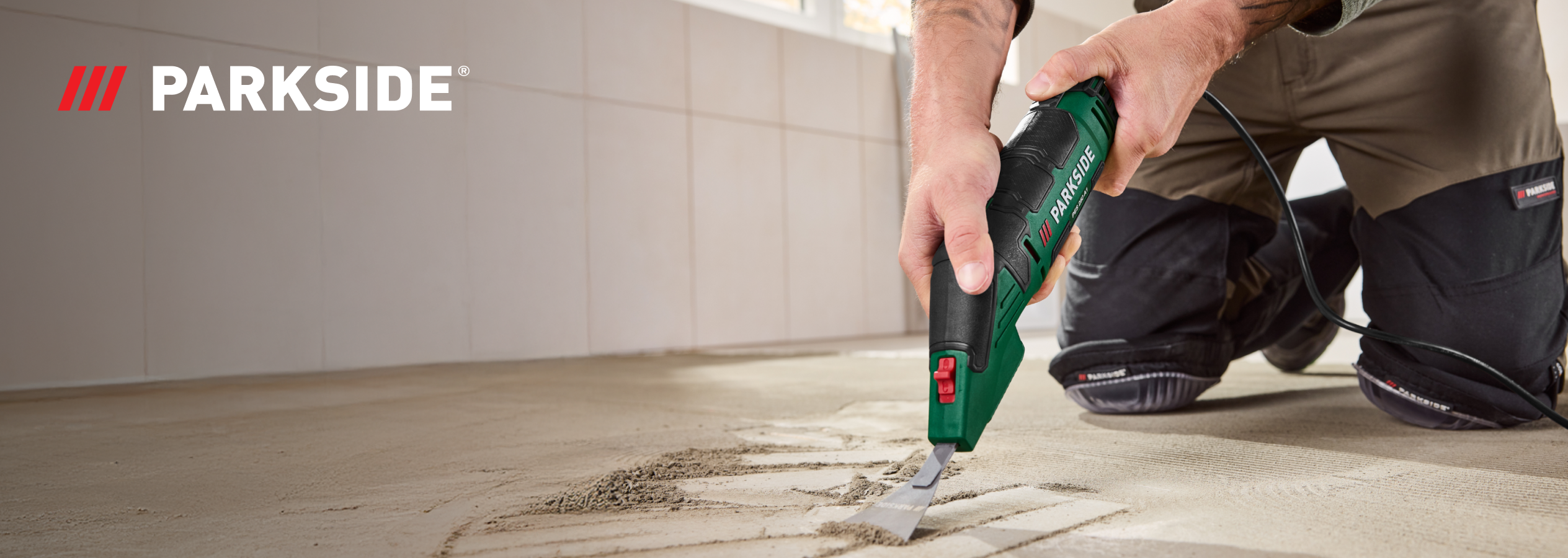Homem a usar uma ferramenta elétrica Parkside para remover argamassa do chão.