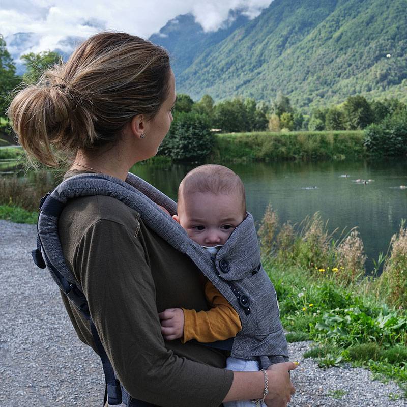 Mãe com bebê em sling ao ar livre.