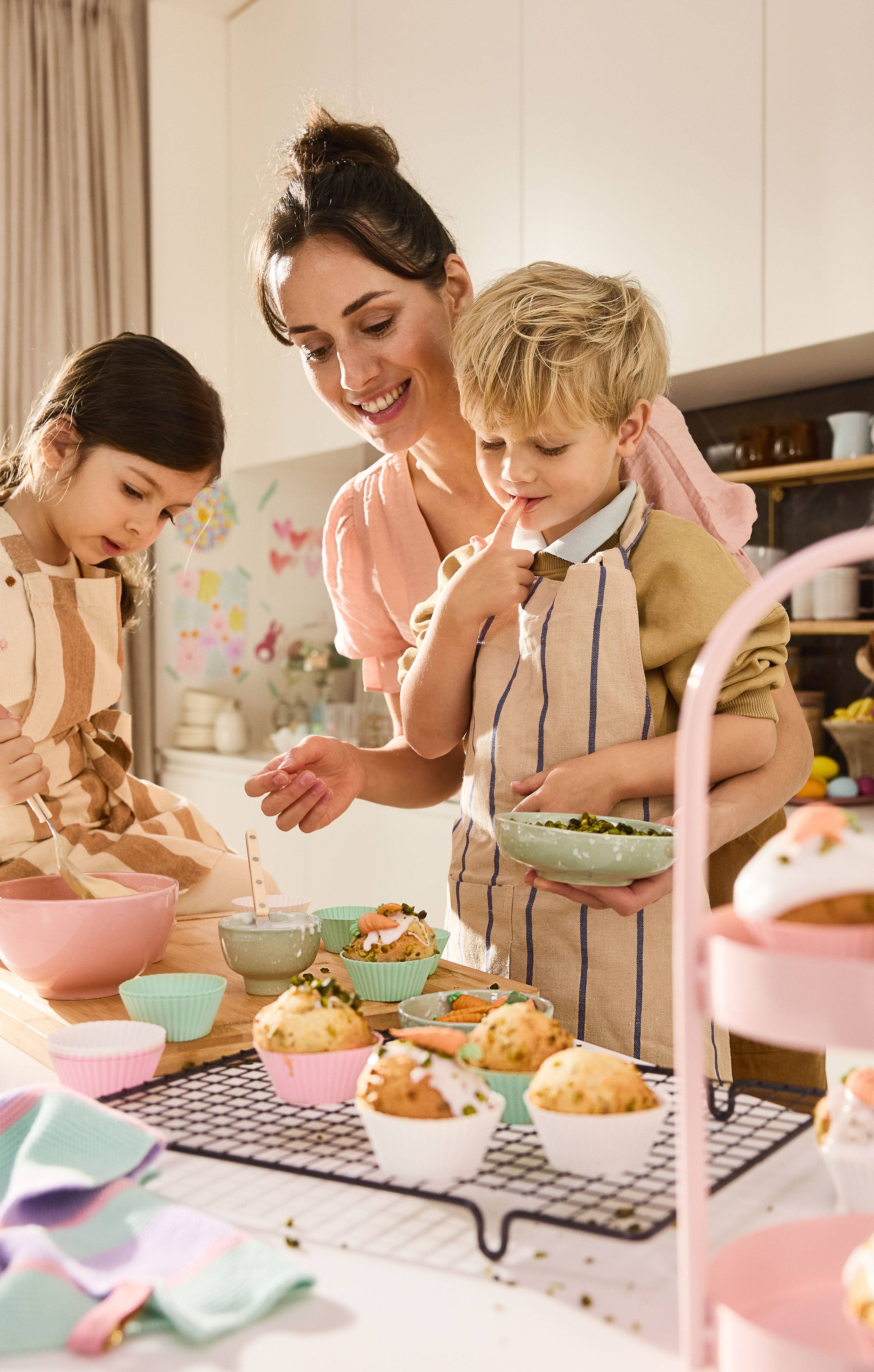 Mãe e filhos decorando muffins de Páscoa com glacê e pistácios.