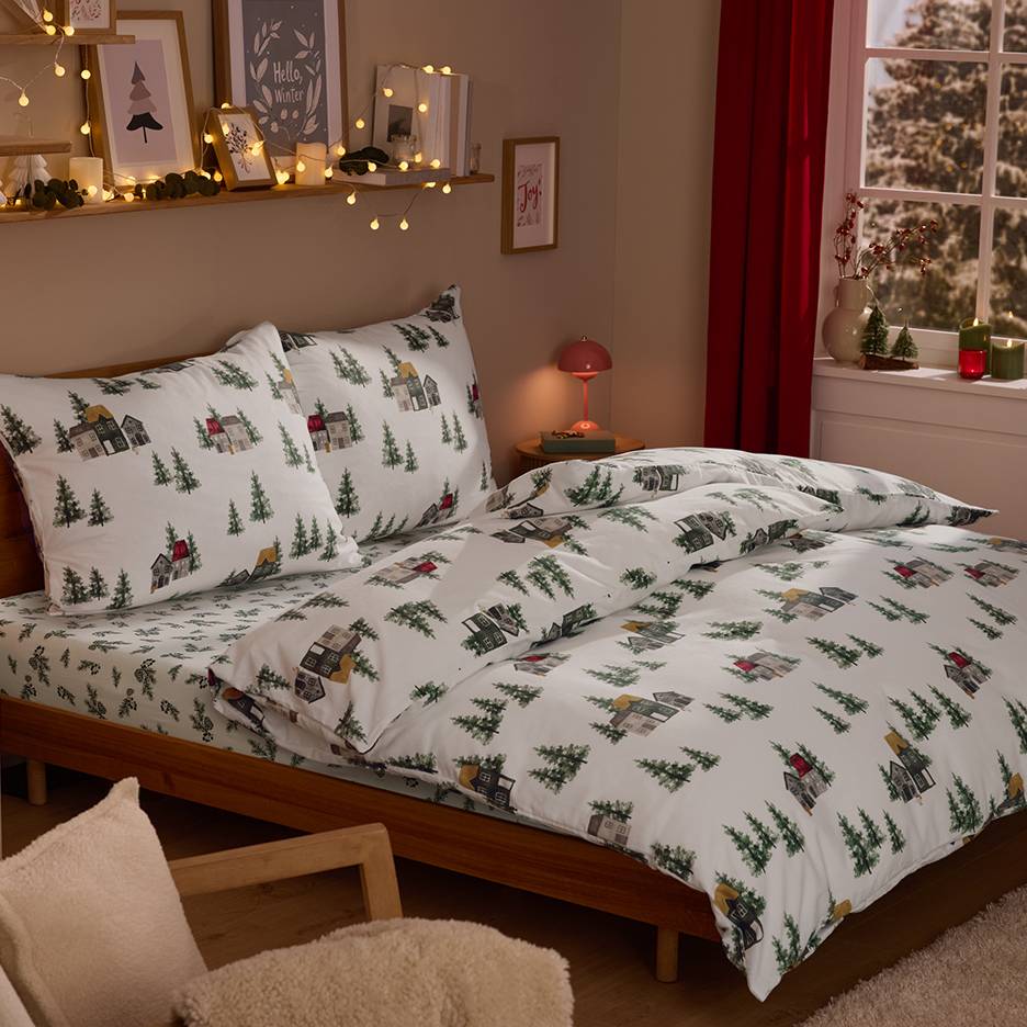 Quarto com roupa de cama com tema de aldeia de inverno, luzes e decorações de Natal.