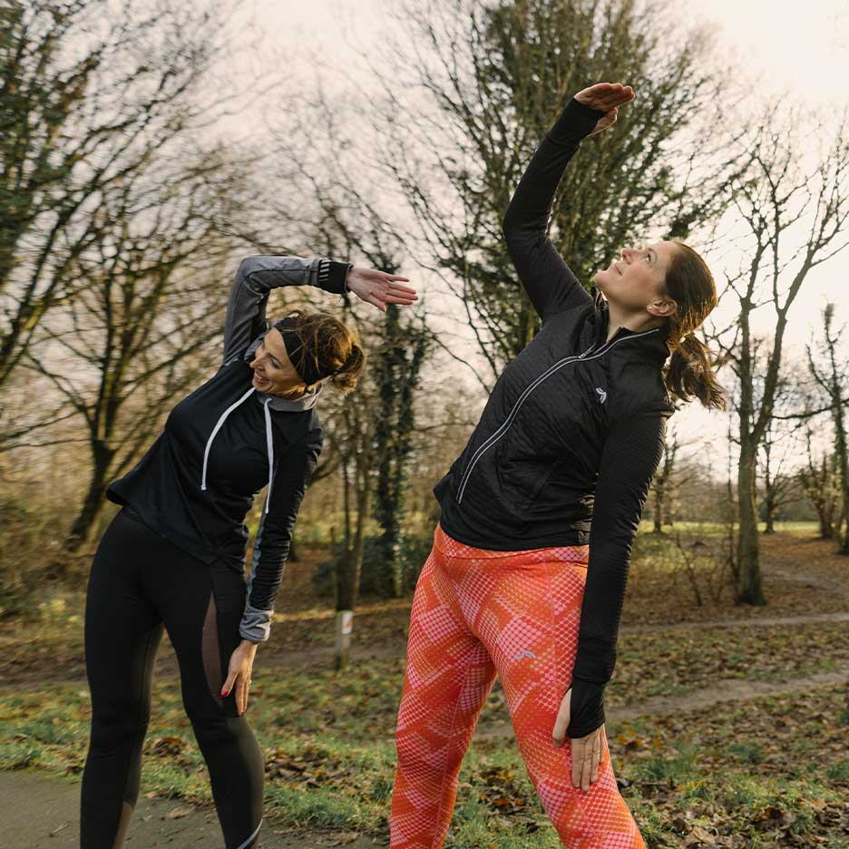 Duas mulheres em roupa desportiva a alongar ao ar livre.
