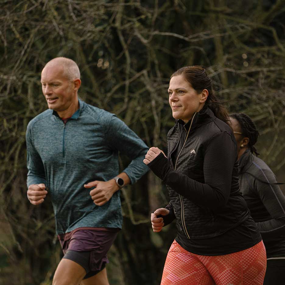 Dois corredores adultos com roupa desportiva a fazer jogging ao ar livre.