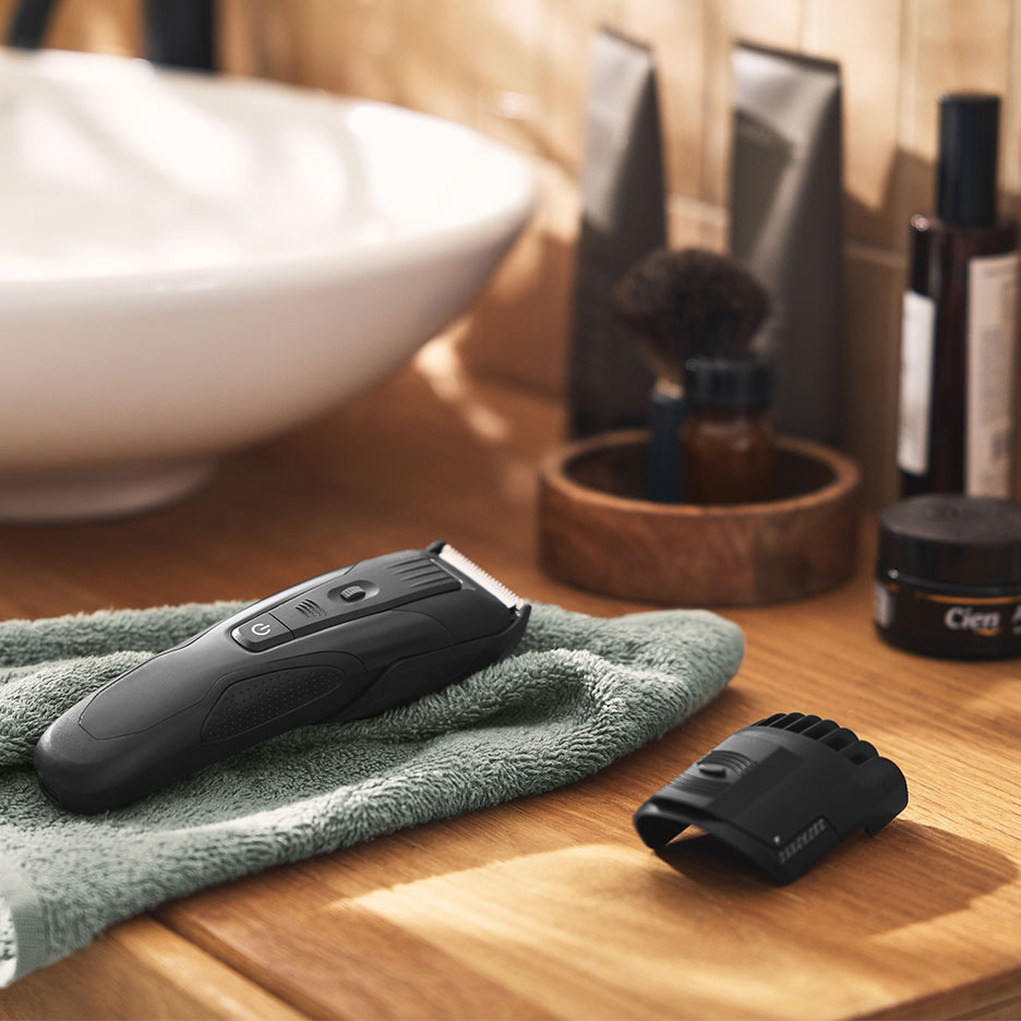 Aparador de cabelo preto sobre uma toalha verde na casa de banho com lavatório e produtos de higiene.