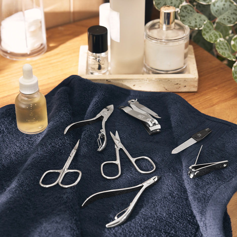 Kit de manicure com corta-unhas, tesouras e limas sobre uma toalha azul-escura.