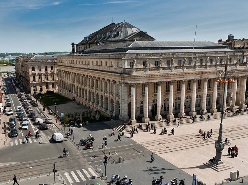 Vista aérea do Grand Théâtre de Bordeaux com pessoas e carros na rua.