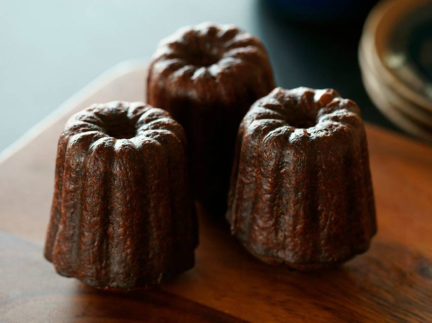 Três canelés de Bordéus numa tábua de madeira.