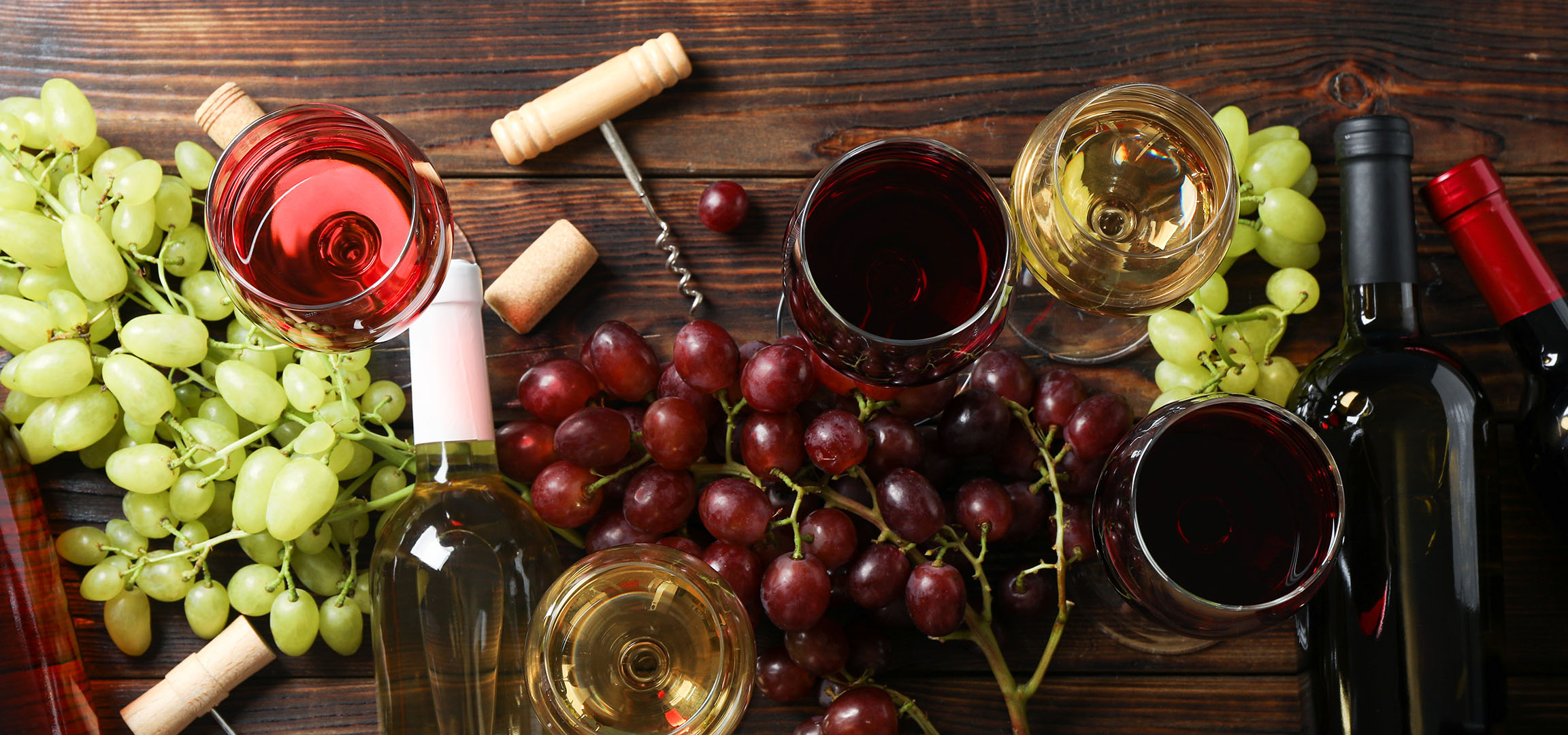 Vários vinhos, uvas e acessórios de vinho numa mesa de madeira.