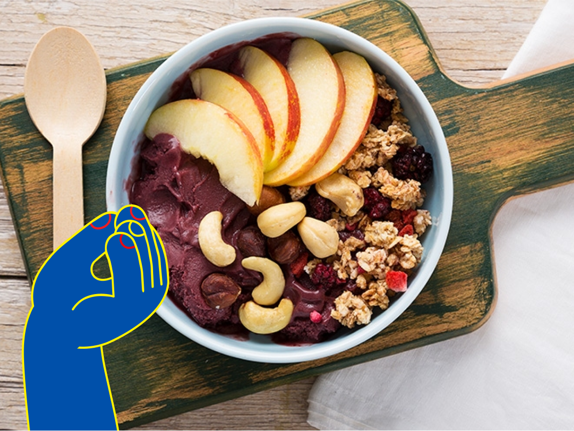 Taça de açaí com maçã, granola e frutos secos, com uma colher de pau e um desenho de mão.