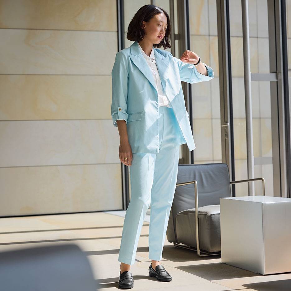 Mulher em fato azul claro com blazer e calças, a usar mocassins pretos.
