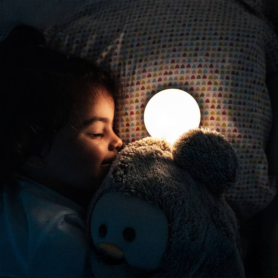 Menina a dormir com peluche e luz noturna acesa.