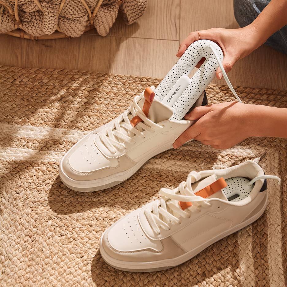 Secador de sapatos Silvercrest em ténis brancos sobre um tapete trançado.