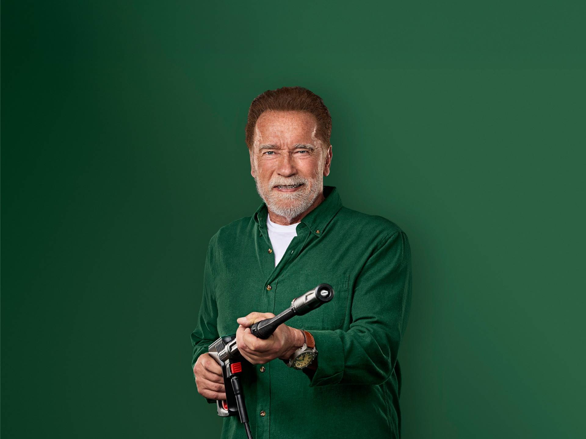 Arnold Schwarzenegger sorri, segurando uma pistola de lavagem de alta pressão.
