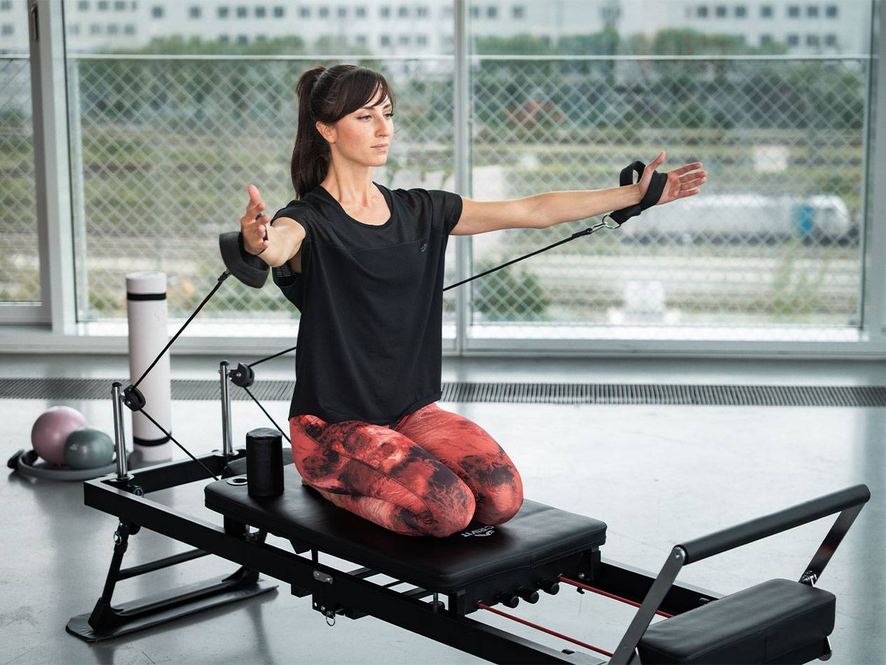 Mulher a fazer Pilates num reformer com bandas de resistência.