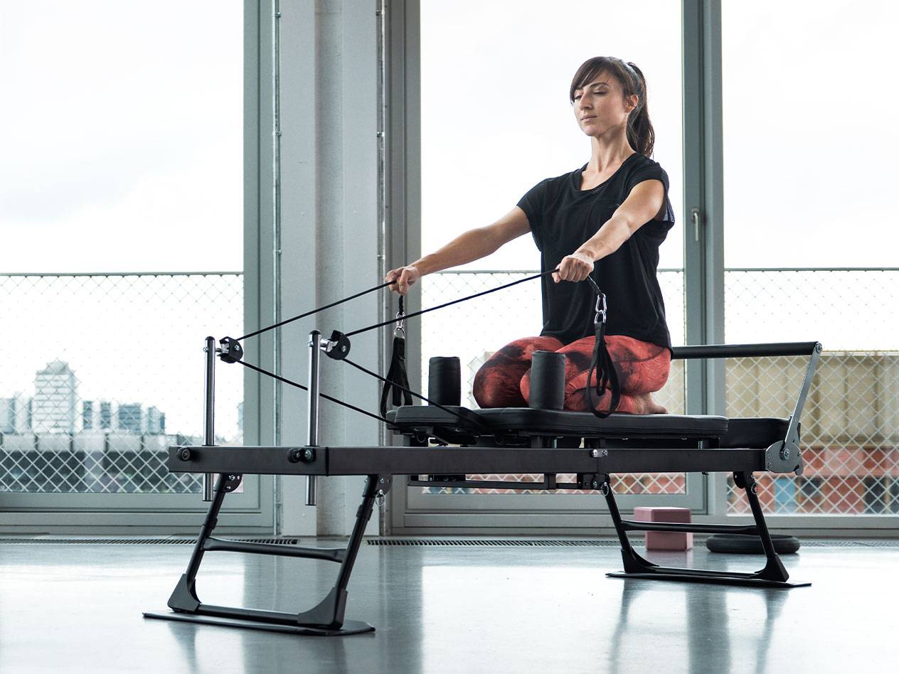 Mulher a fazer exercício de Pilates numa máquina reformer com fundo de cidade.
