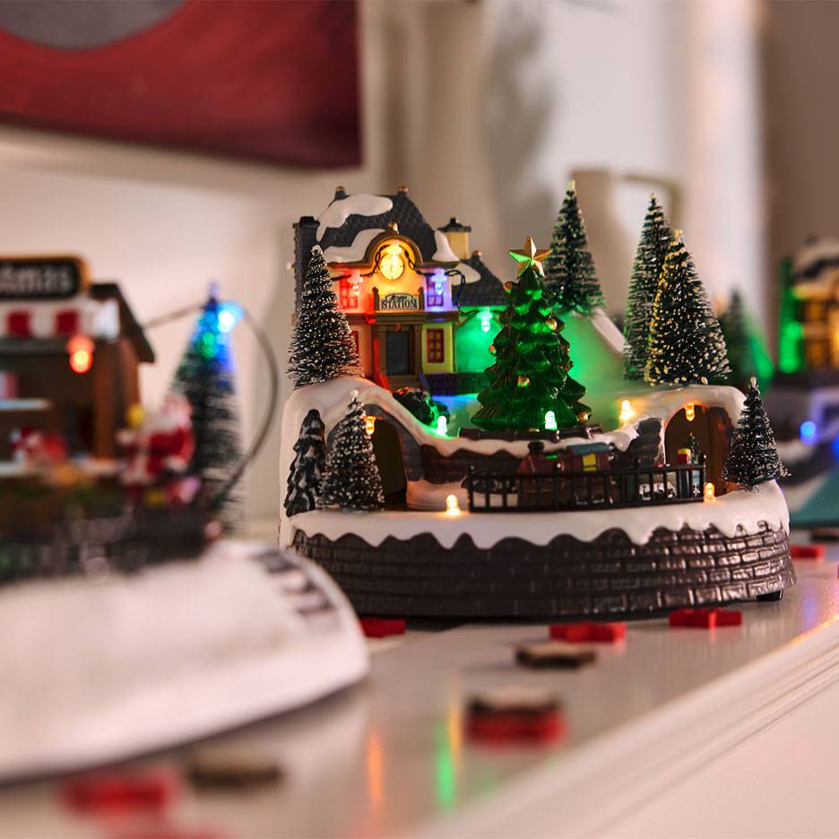 Aldeia de Natal com estação iluminada, árvores e comboio em miniatura.