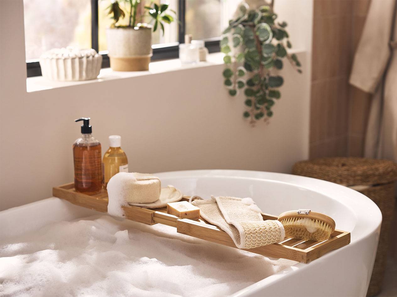 Tabuleiro de banho de bambu com produtos de banho, esponjas e escovas sobre um banho de espuma.