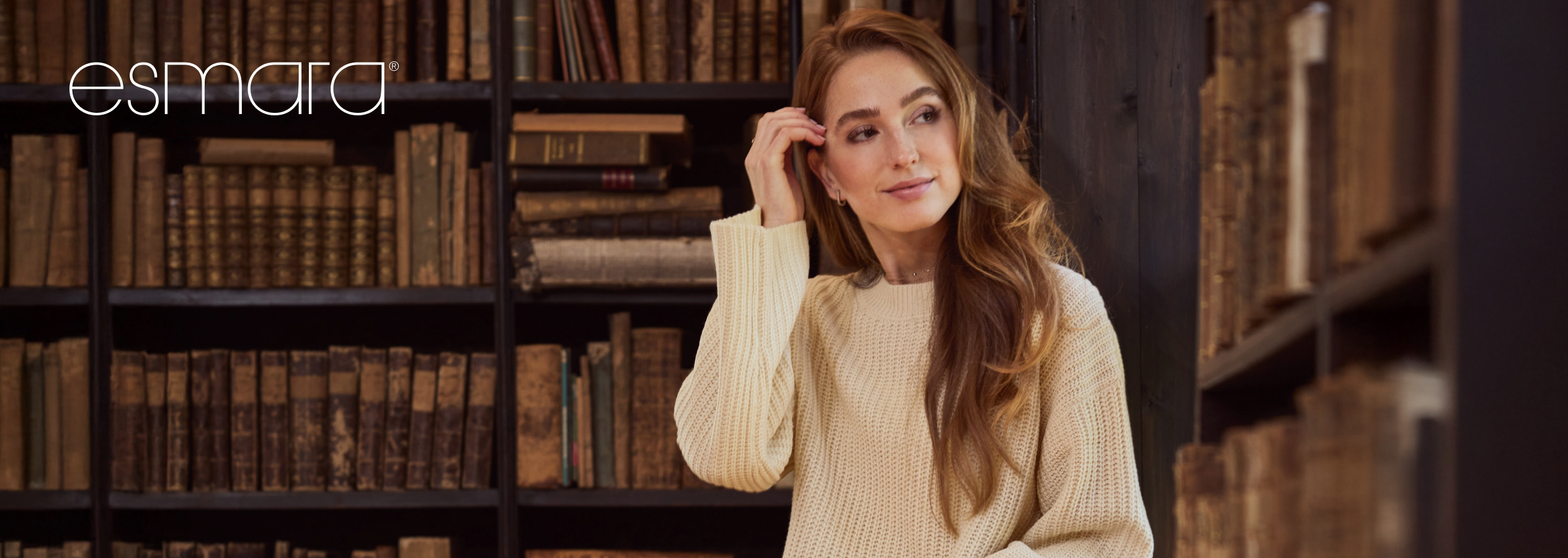 Mulher de camisola Esmara bege em biblioteca com livros antigos.