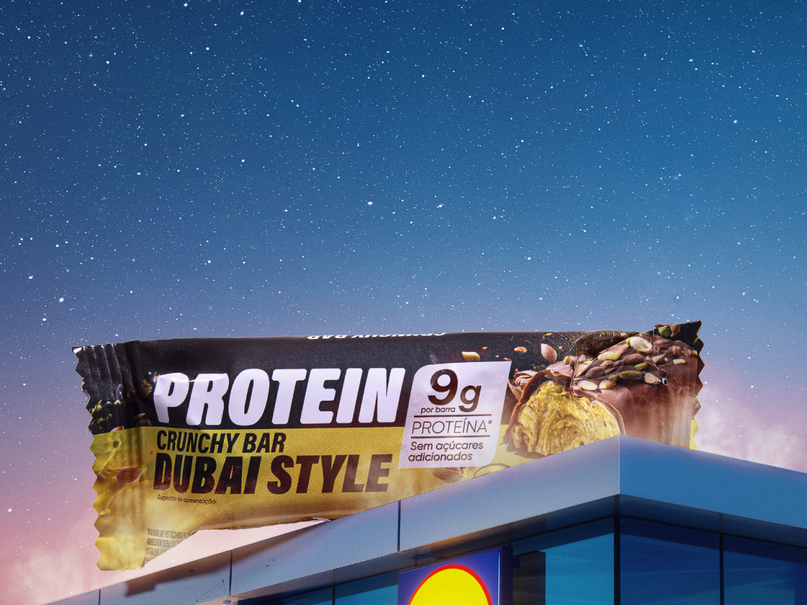 Barra de proteína 'Dubai Style' com 9g de proteína, sem açúcares adicionados, sobre um edifício Lidl sob um céu estrelado.