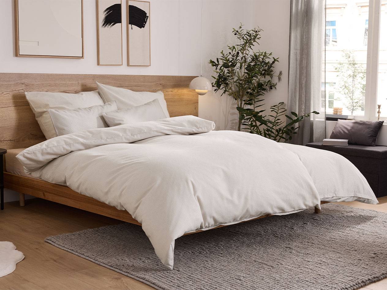 Quarto com cama de madeira, roupa de cama branca e tapete cinzento.