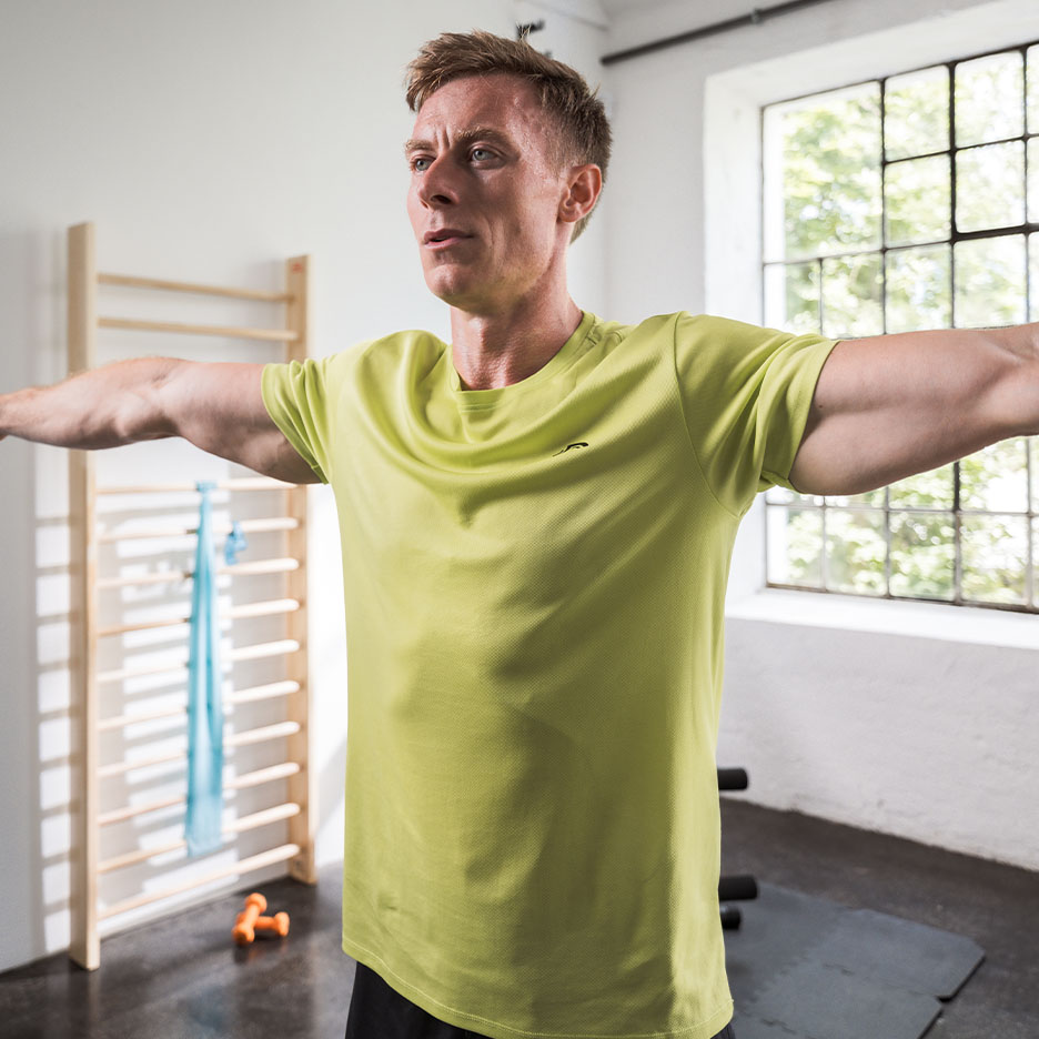 Homem de camiseta atlética verde se exercitando em uma academia.