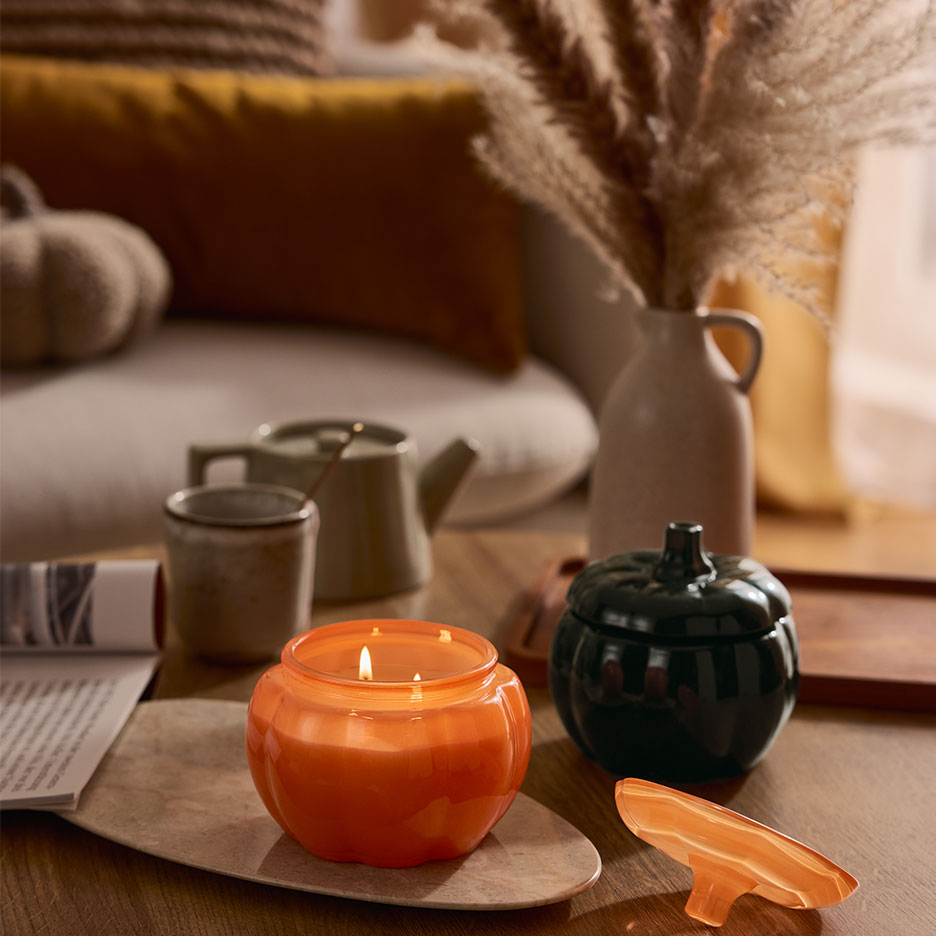 Vela e recipiente em forma de abóbora em uma mesa de centro com decoração de outono.