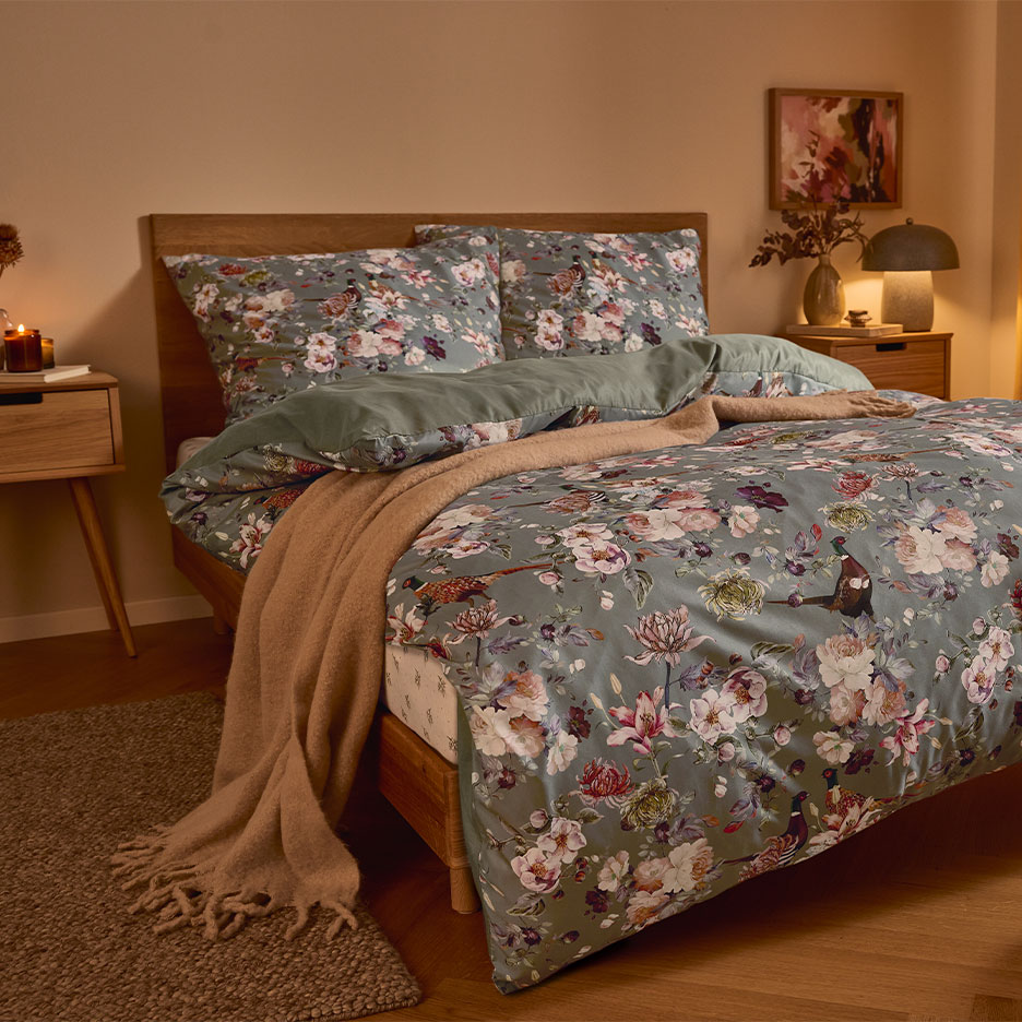 Cama de madeira com roupa de cama floral verde e um cobertor marrom.