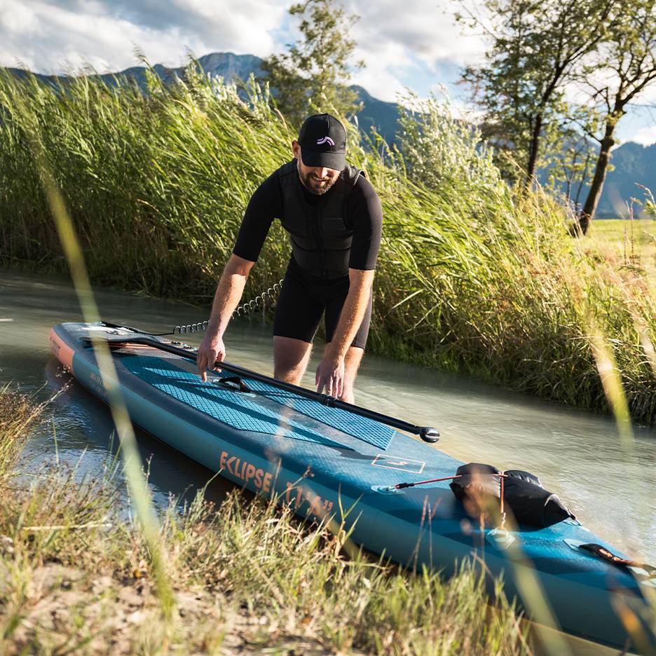Homem de fato de mergulho preto a preparar-se para paddleboard, prancha na água