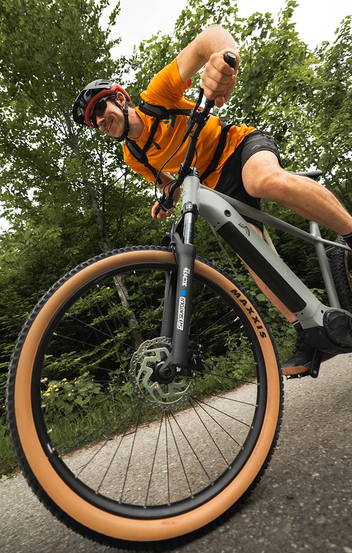 Um homem anda de bicicleta elétrica Maxxis cinzenta numa floresta.